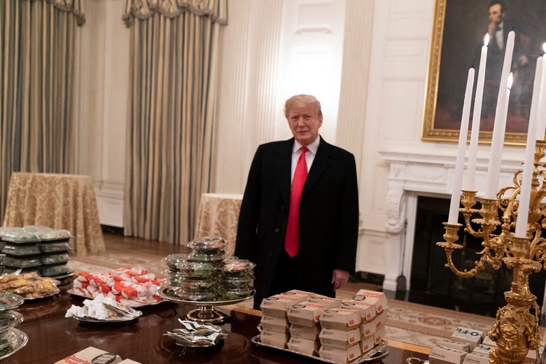 Trump stands in front of a table covered in fast food with a portrait of Abraham Lincoln behind him.